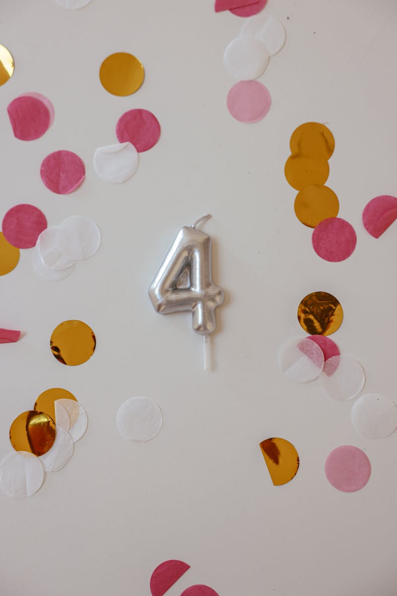 A silver number 4 balloon surrounded by pink, gold, and white confetti, capturing a festive celebration theme.