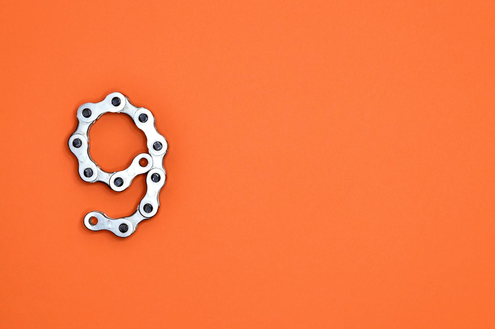 A metal chain shaped like the number nine against a vibrant orange background with copy space.