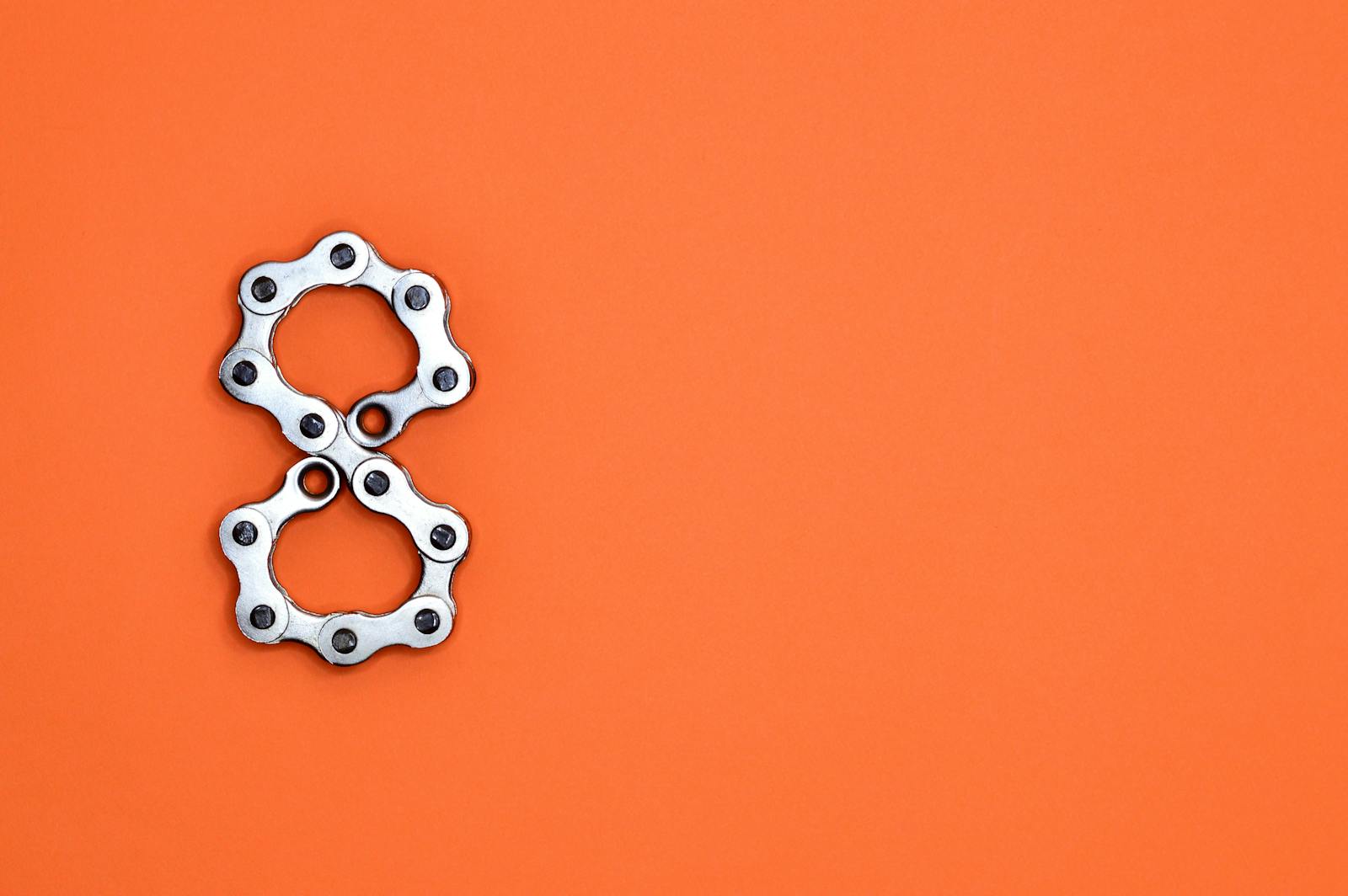 Creative arrangement of bicycle chain links in the shape of the number eight on a bright orange background.