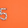 Creative arrangement of a chrome bicycle chain forming the number 5 on a vibrant orange background.