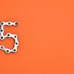 Creative arrangement of a chrome bicycle chain forming the number 5 on a vibrant orange background.