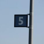 Close-up of metal pole with number 5 sign against a clear blue sky.