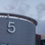 A modern building facade featuring the number 5 against a cloudy sky.