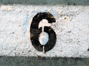 Close-up of a weathered number six painted on a cracked road surface.