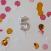 A silver number 5 candle surrounded by colorful confetti, perfect for birthday celebrations.