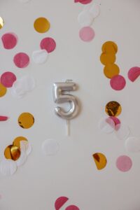 A silver number 5 candle surrounded by colorful confetti, perfect for birthday celebrations.